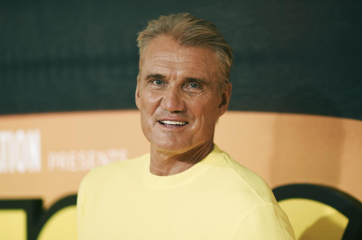 A tanned man in a yellow shirt smiling and looking over his left shoulder.