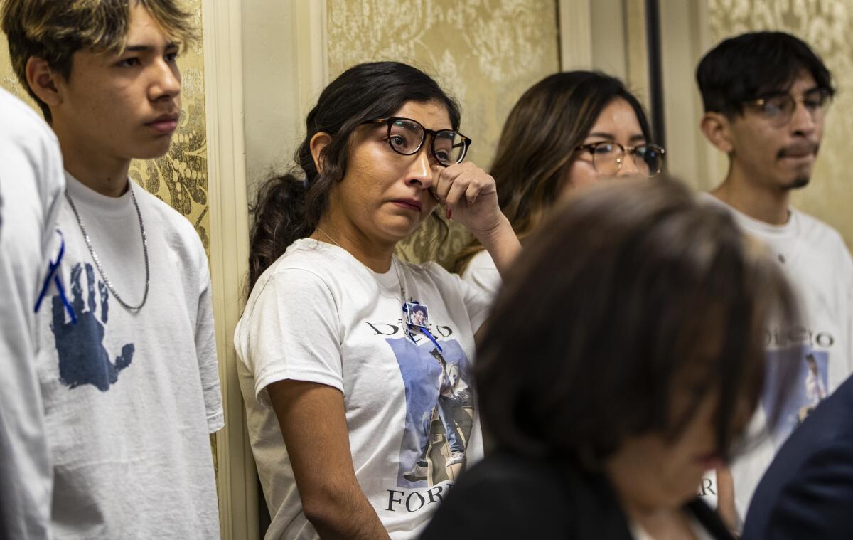 A teenage girl wipes away tears while standing among other students