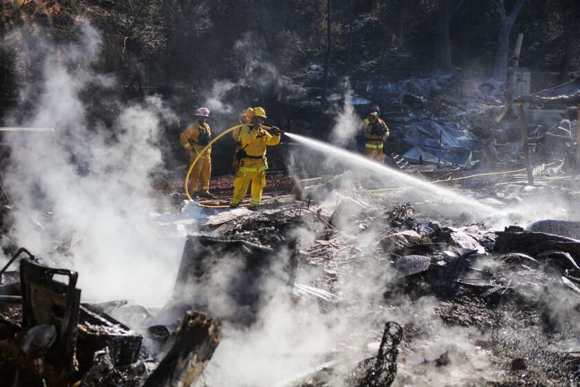 Firefighters work to contain embers on the remains of a house destroyed by the Clayton fire in Lower Lake, California.