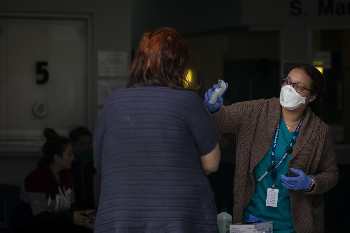 During the coroniavirus pandemic Wendy Urquiza, right, medical assistant talks with people and checks their temperature at the entrance to South Central Family Health Center (SCFHC) on Wednesday, April 8, 2020 in Los Angeles.