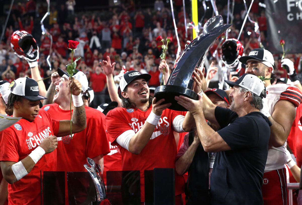 Utah coach Kyle Whittingham, right, hands the trophy to quarterback Cameron Rising, center, after Utah defeated Southern California 47-24 in the Pac-12 Conference championship NCAA college football game Friday, Dec. 2, 2022, in Las Vegas. (AP Photo/Steve Marcus)