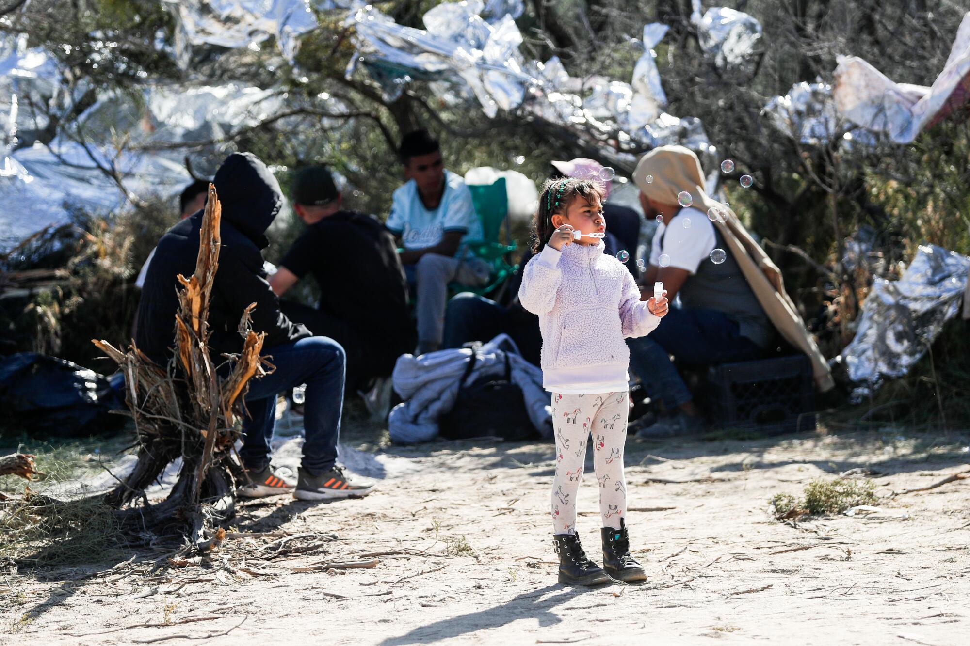 Luciana Eyleen, 7, from Colombia, blows bubbles near other migrants in a makeshift campsite