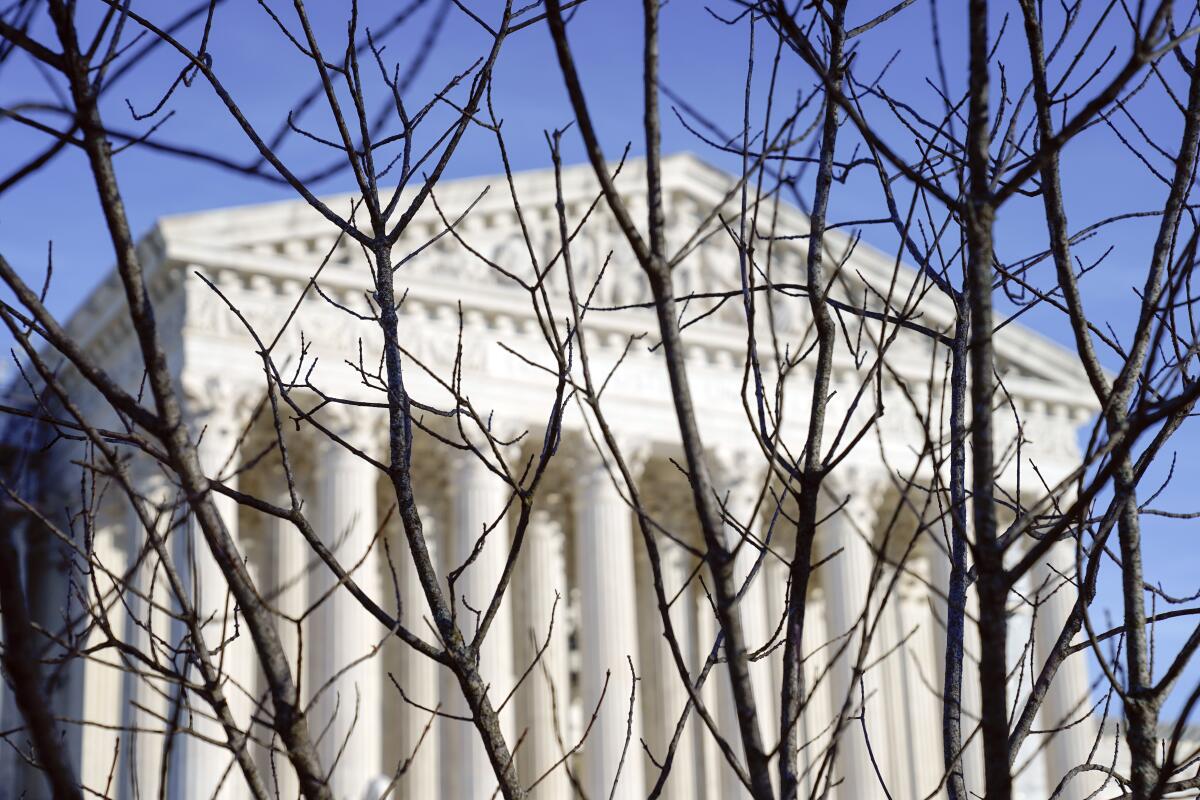 The U.S. Supreme Court seen against a bright blue sky through bare tree branches.