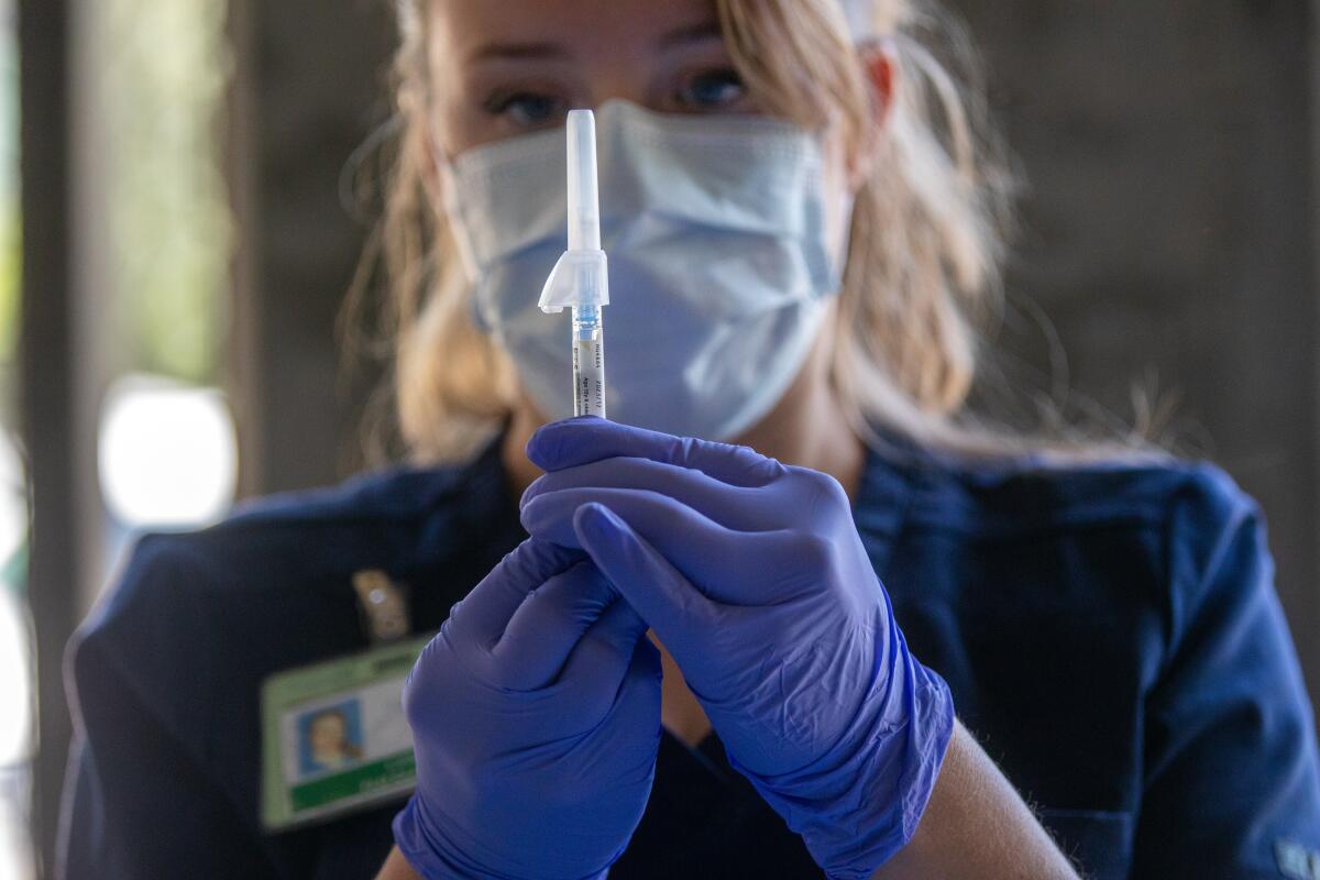 A nurse wears a mask and gloves while preparing a syringe 