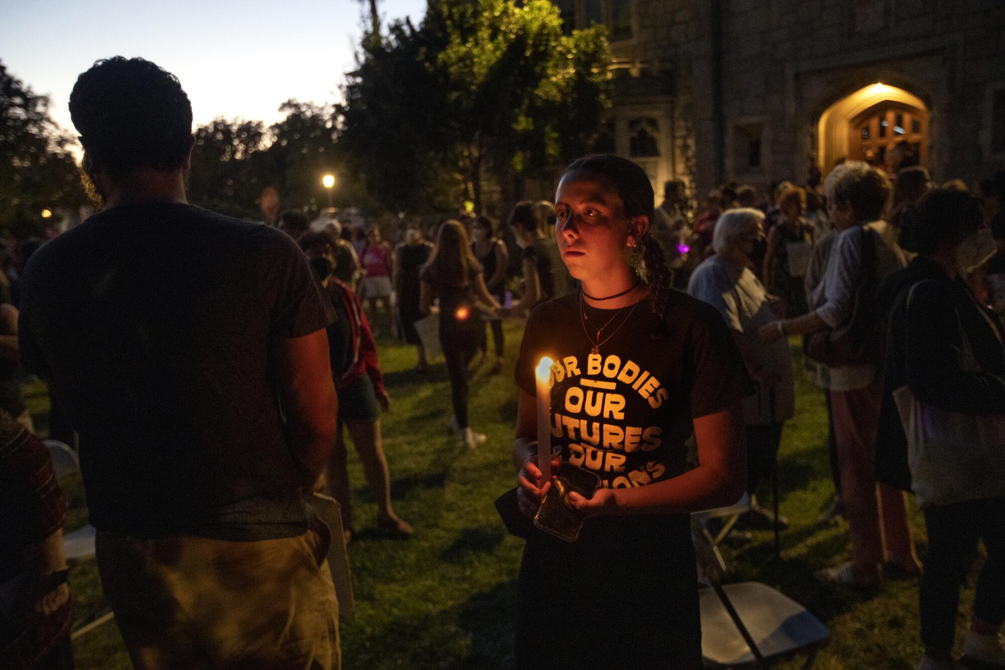 A teenager surrounded by other protesters holds a candle