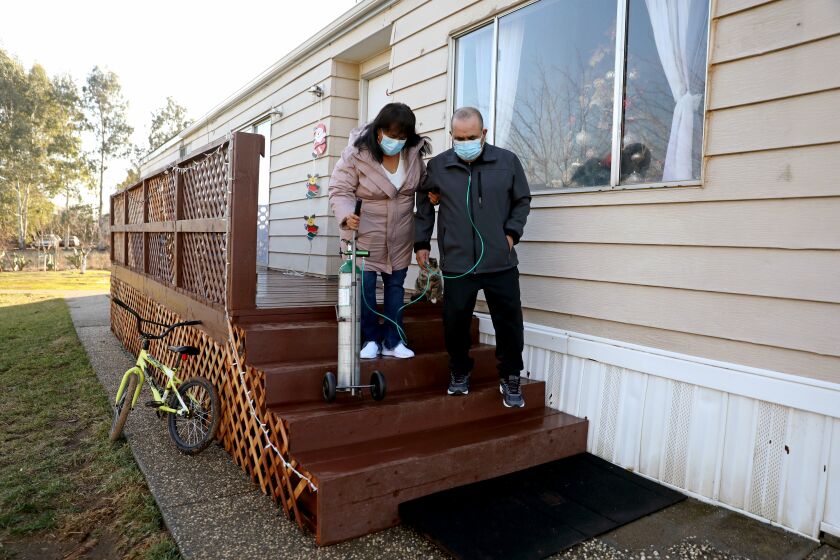 CORNING, CA - JANUARY 08: Maria Marin, 58, helps her husband David Marin, 56, with his oxygen tank, where extended family of nine live at their trailer home on Friday, Jan. 8, 2021 in Corning, CA. The Marin family of nine all contracted COVID-19 in July 2020. David was admitted to ICU where he was in an induced coma for 24 of the 48 days. Marin is still suffering long term repercussions from COVID-19. How the COVID-19 pandemic has affected small towns in rural Tehama County, with a population of 65,000 people. As of Jan. 6th the Tehama County has 3,586 positive, 19,490 negative test results and 40 deaths. (Gary Coronado / Los Angeles Times)