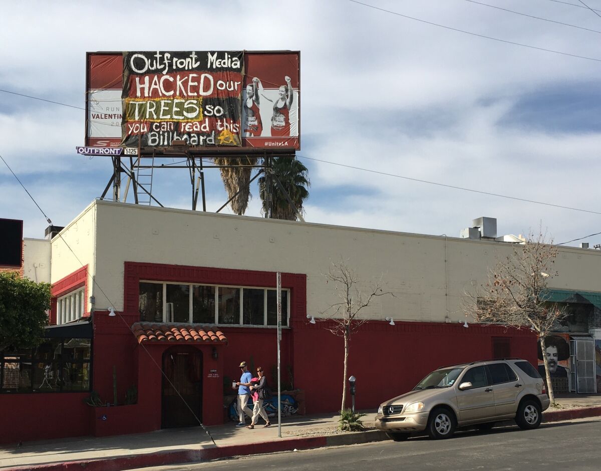 A banner was placed over a billboard above El Condor restaurant on Sunset Boulevard in Silver Lake. Activists have criticized the billboard company, Outfront Media, for cutting back several trees without city permits.