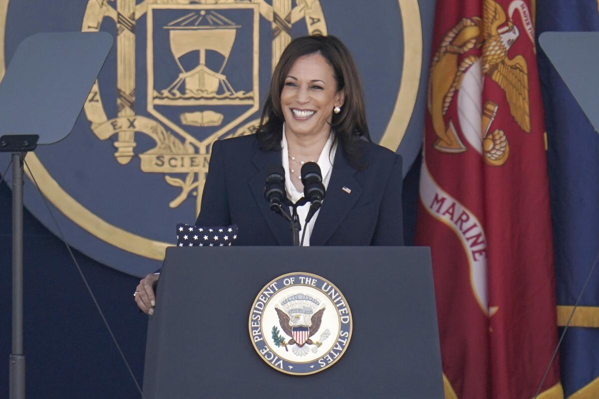 Kamala Harris speaking at a lectern with the Marine flag behind her