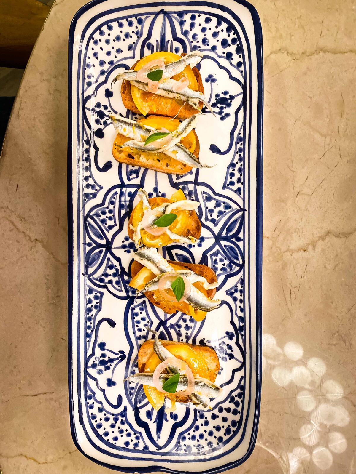 Crostini with tiny anchovies, shaved coins of tart preserved oranges and shaved ricotta salata