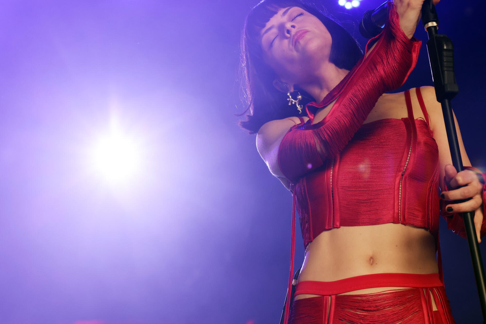 A woman in a red outfit closes her eyes as light shines beside her.