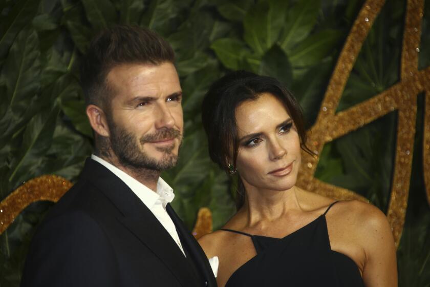 David Beckham in a suit without a tie posing next to Victoria Beckham in a black dress