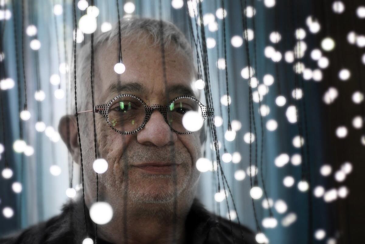 A man wearing round glasses stands under dangling string lights