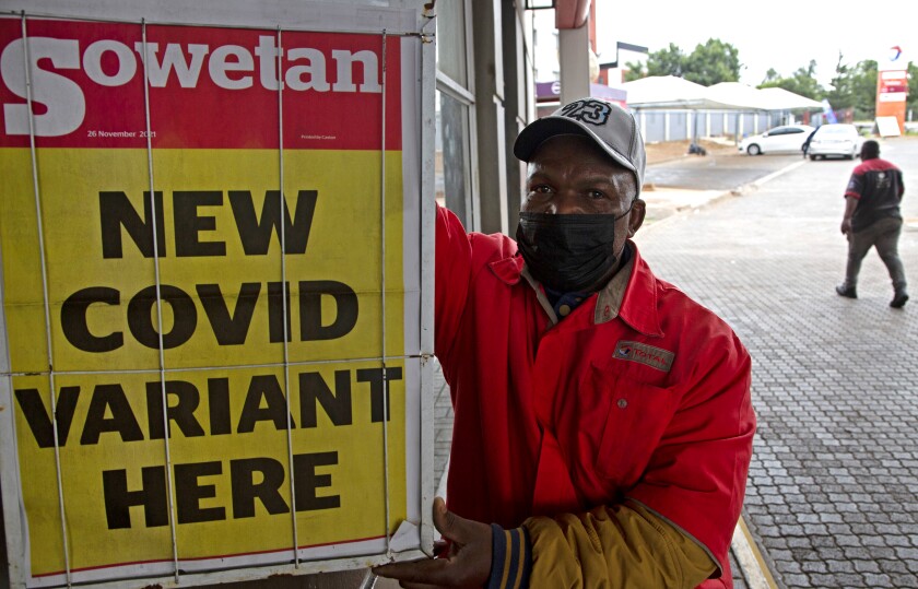 A man in a mask stands alongside a newspaper with the headline "New COVID variant here."