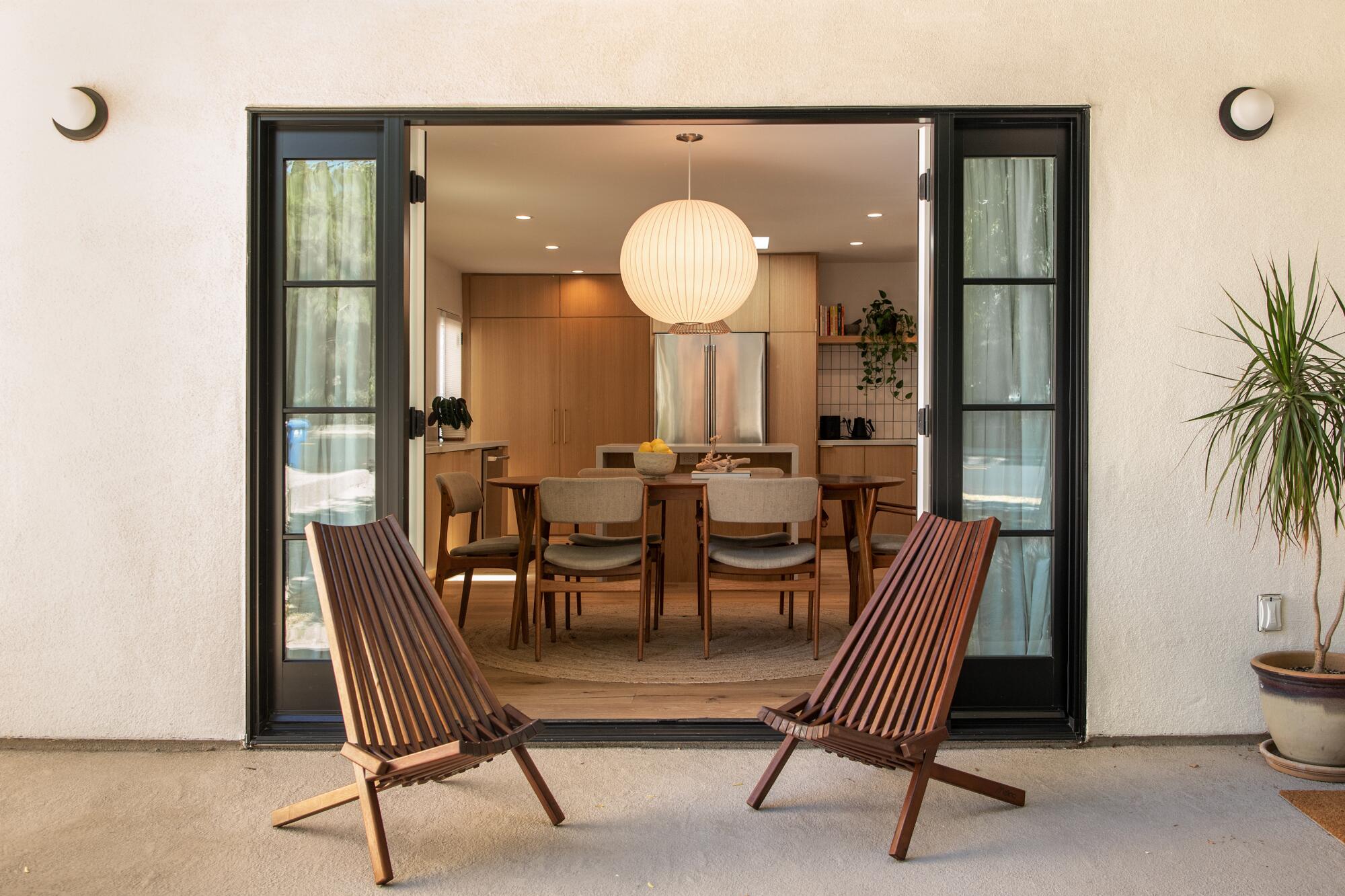 Two lounge chairs in front of open doors with the kitchen and dining room in the background. 