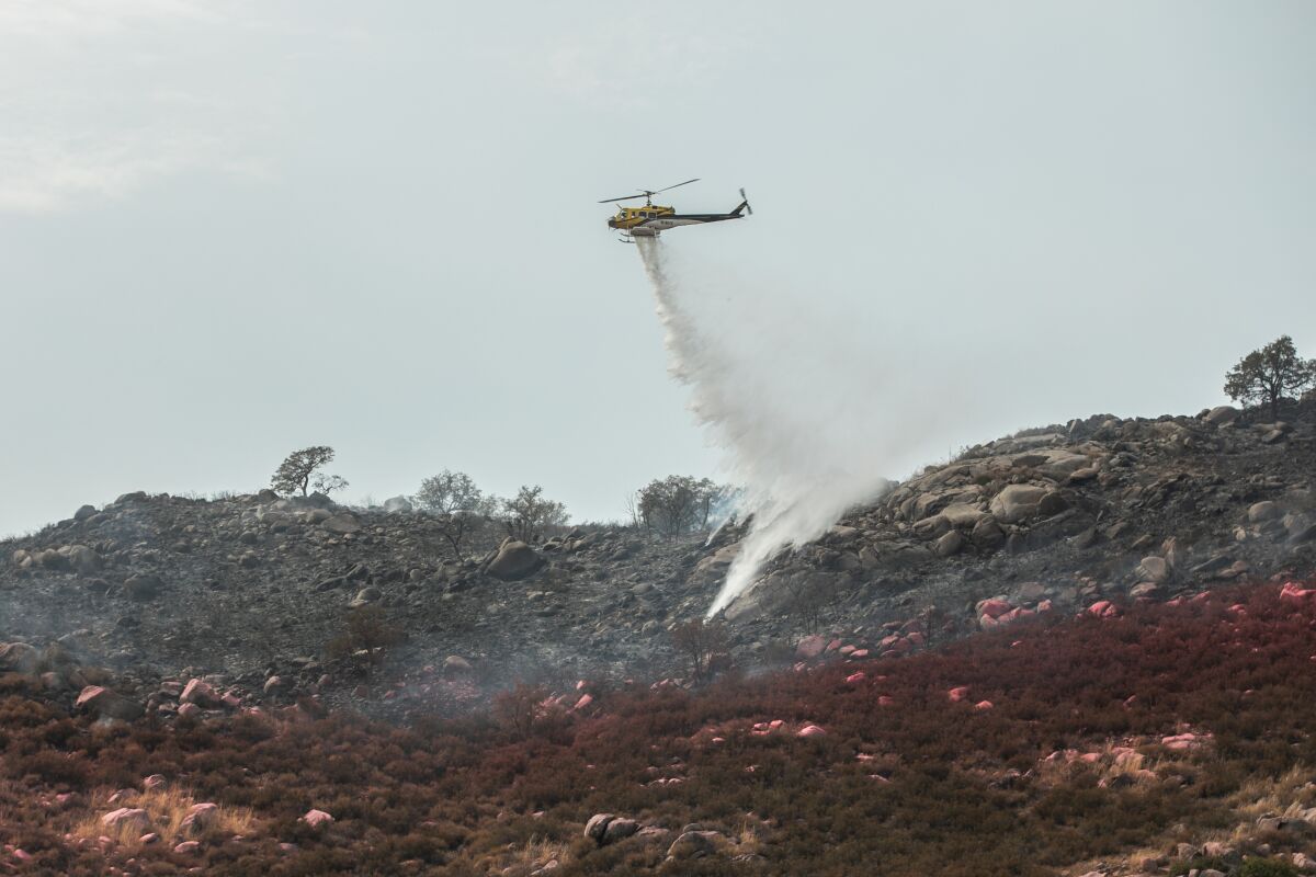 A helicopter drops water to contain the Casner Fire near Rancho Ballena Lane in Ramona, CA on Wednesday, July 27, 2022.