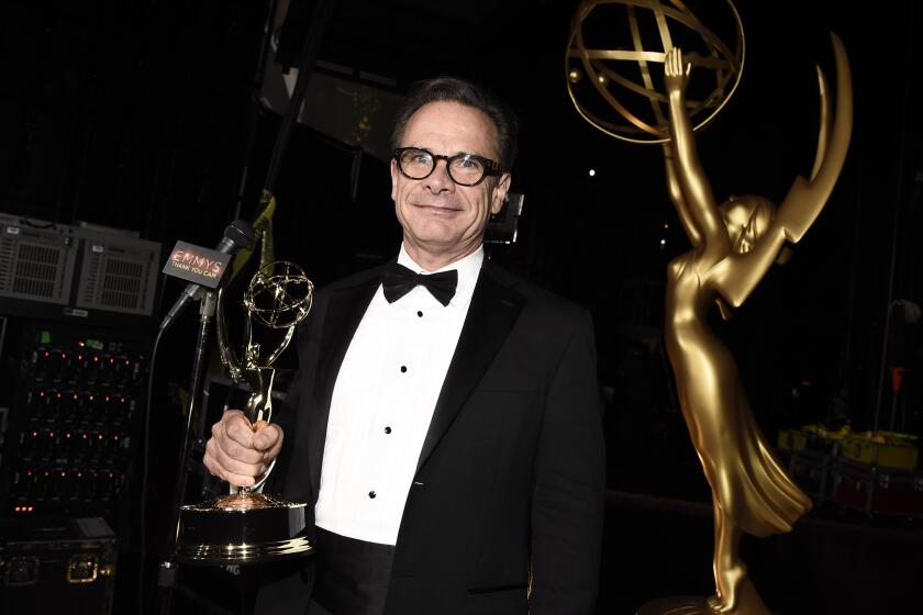 A man wearing glasses and a tuxedo holding an Emmy trophy