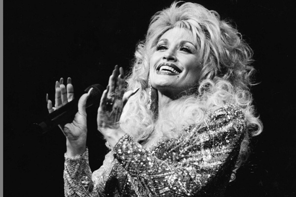 Dolly Parton, in a bedazzled gown, holds a microphone and smiles.