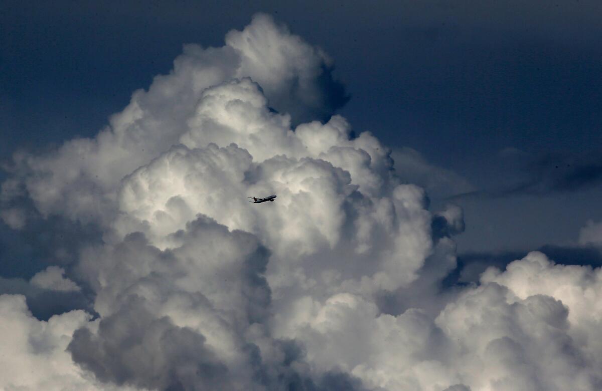 A plane in the distance flying against large, heavy clouds