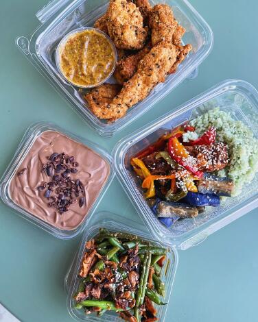 Four clear plastic containers with assorted foods in them, including chicken tenders and chocolate tofu pudding