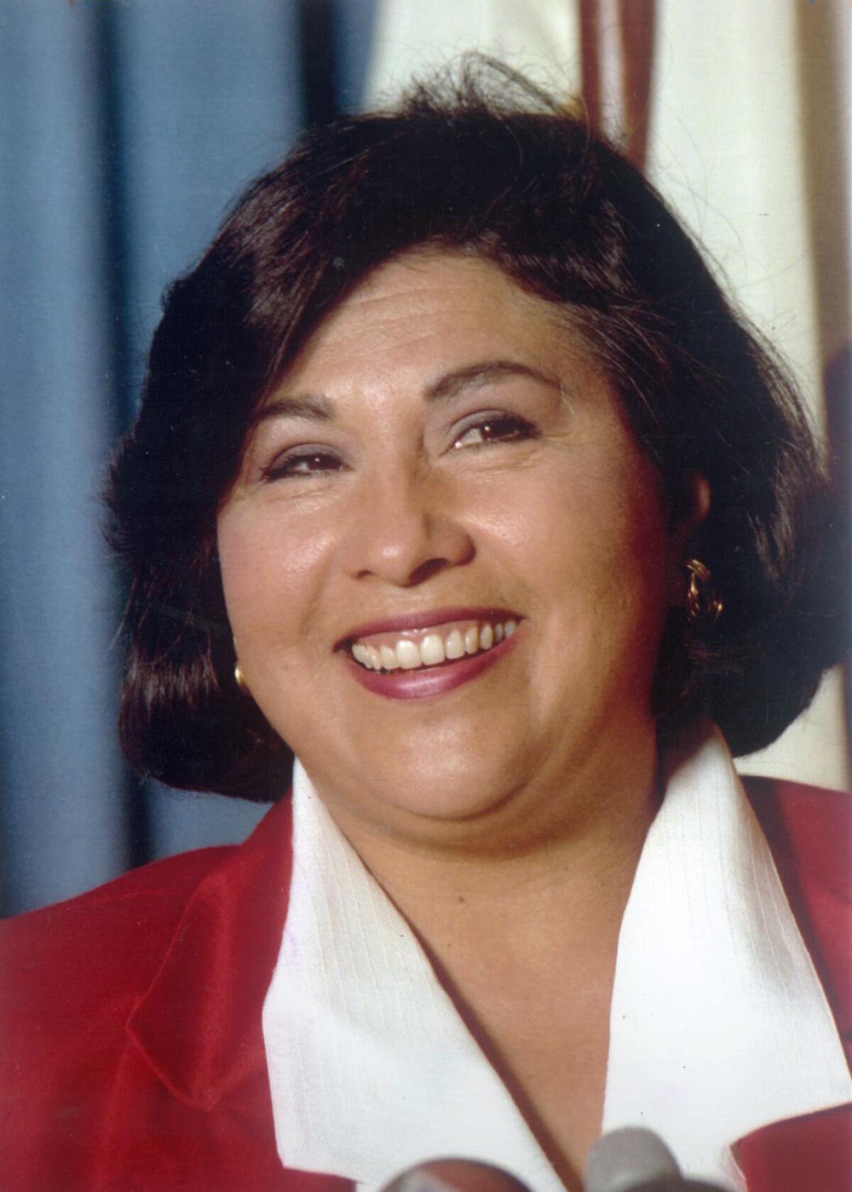 A head-and-shoulders vertical portrait of a smiling woman with chin-length dark brown hair. 