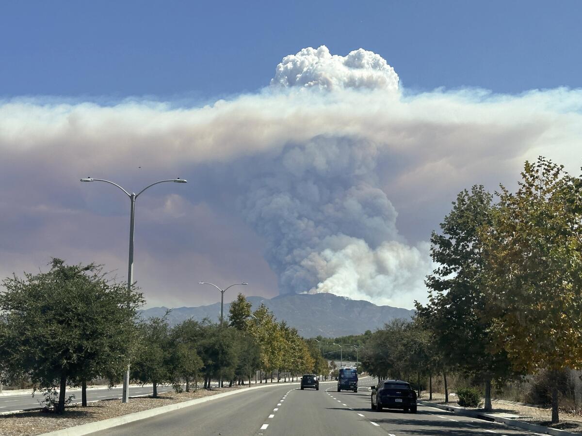 Una columna de humo generada por el incendio Airport se eleva sobre la cima de una montaña,