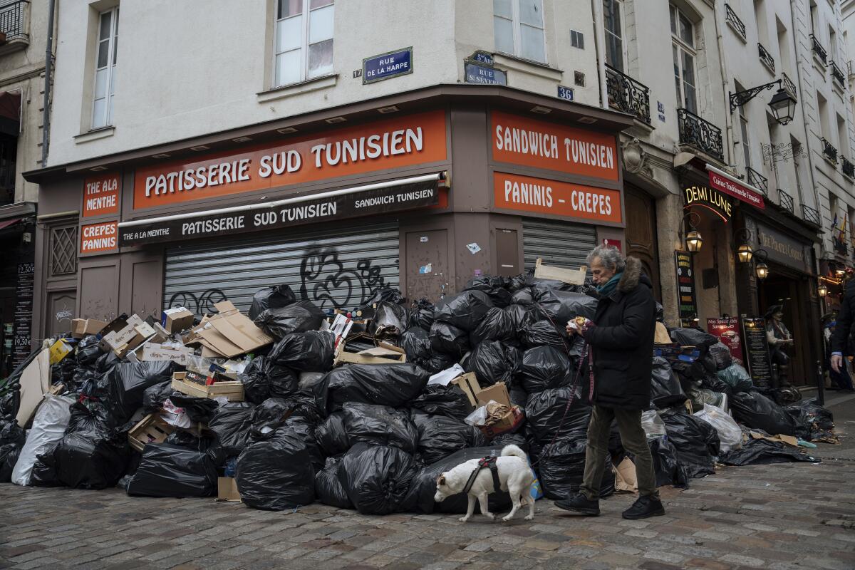 Un hombre pasa caminando junto a montones de basura en París, el 13 de marzo de 2023. (AP Foto/Lewis Joly)