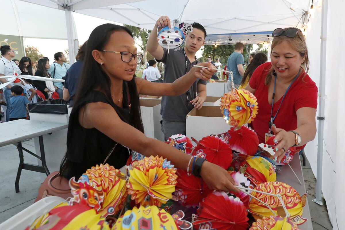 Kristina Le-Nguyen, right, Elise Ho, left, and Hiep Tran — all volunteers with CalOptima — arrange paper lanterns before handing them out for free with moon cake during the Moon Festival Saturday at Mile Square Park's Freedom Hall.