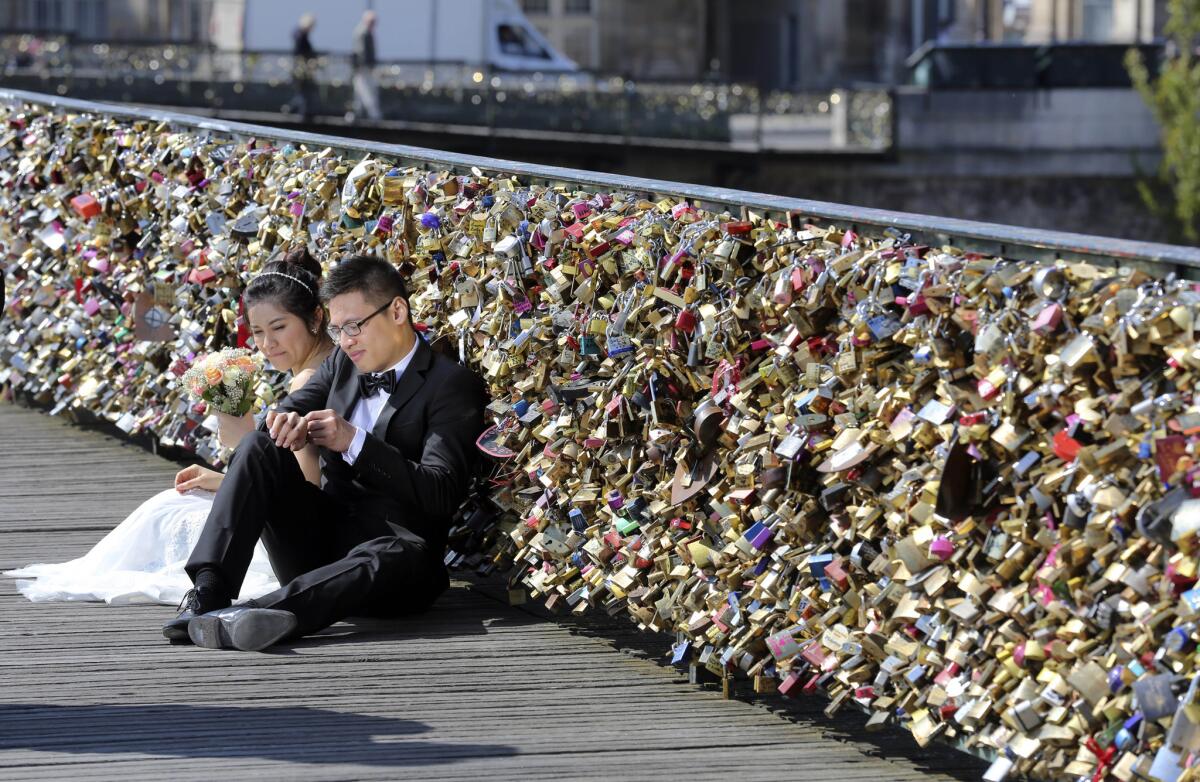 Unos recién casados visitan el Pont des Arts en París, Francia, el 16 de abril de 2014. La ciudad planea desmantelar el lunes 1 de junio el popular puente donde miles de enamorados colocan candados como símbolo de amor, después que el año pasado se cayera un pedazo de la reja debido al peso de los candados del amor. (Foto AP/Remy de la Mauviniere, File)