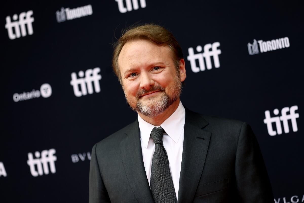 A smiling, goateed man in a dark suit stands before a TIFF step-and-repeat banner.