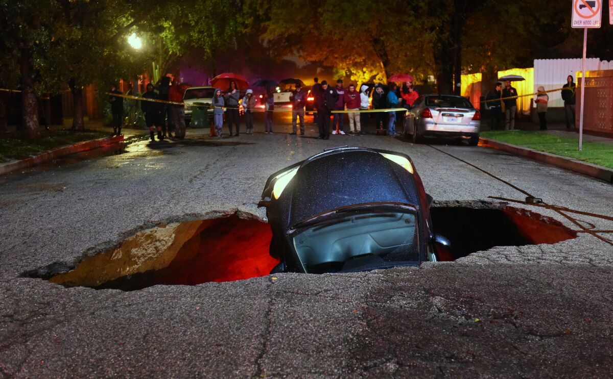 A car sits in a sinkhole on Woodbridge Street near Laurel Canyon Boulevard in Studio City following Friday's rain.