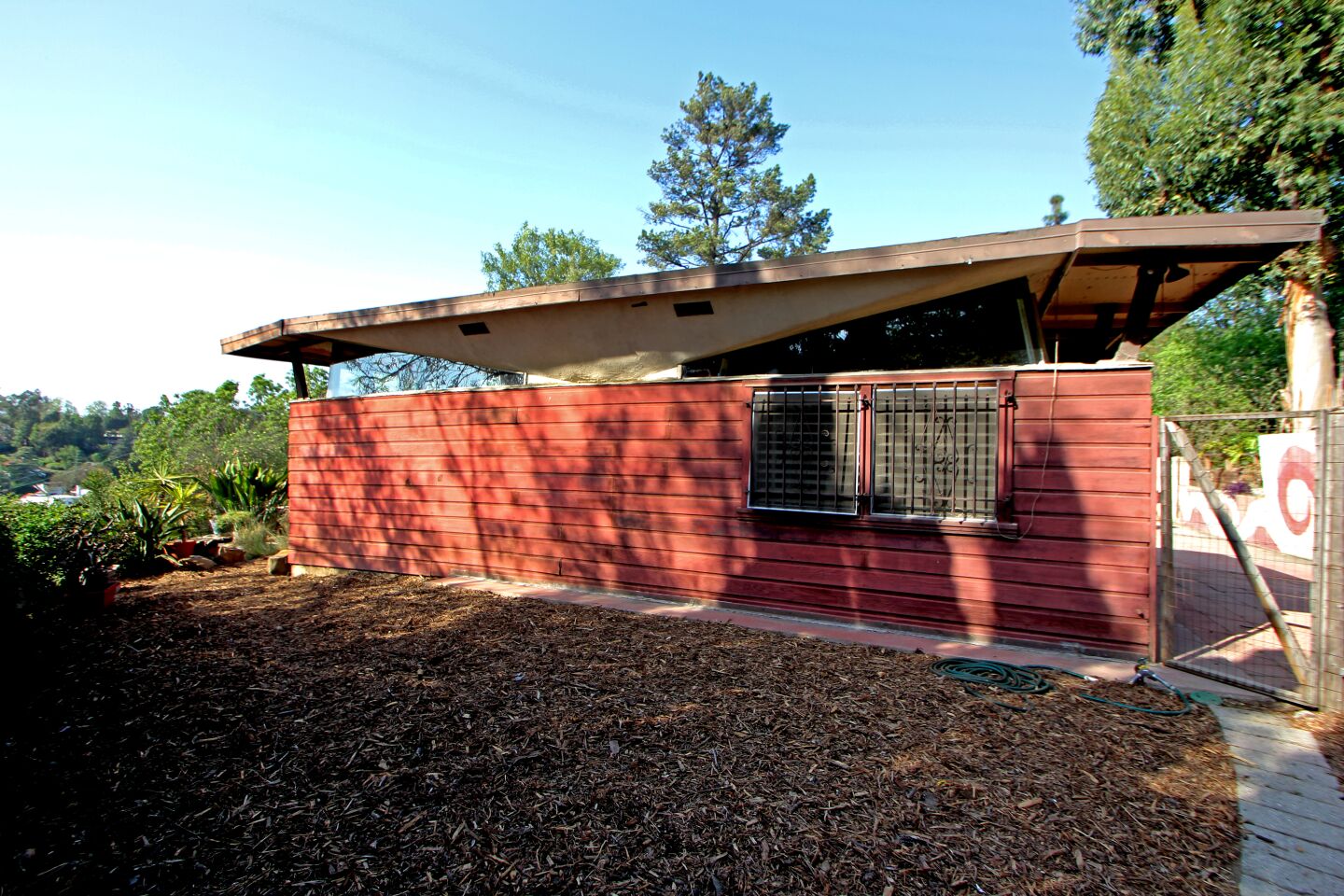 BEFORE - EXTERIOR: The home had been a rental for years and suffered water damage — the soaring roof design, the unmaintained glass walls and doors, and the slab-on-grade foundation that had settled all allowed flooding during rains.