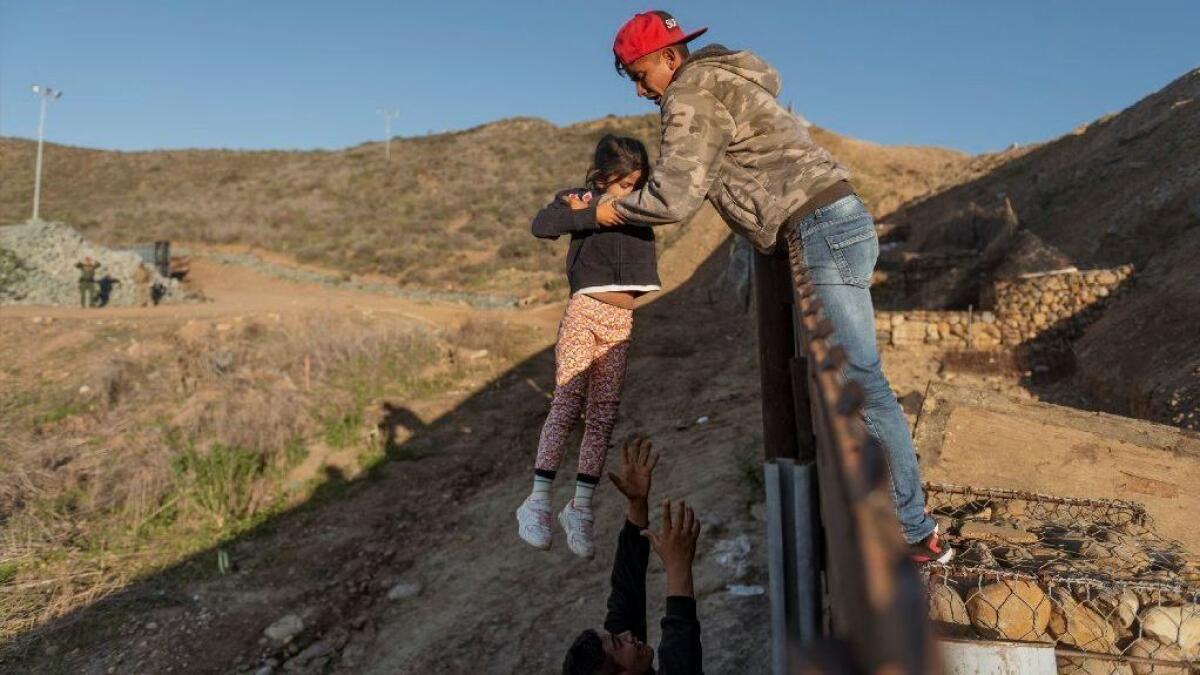 A migrant child from Honduras is passed to her father after he jumped the border fence to get into the United States from Tijuana on Jan. 3.