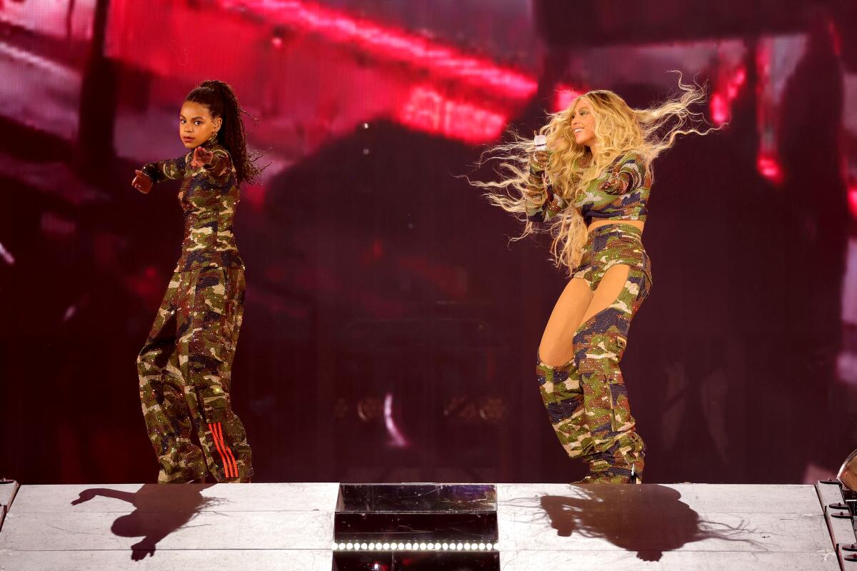 Blue Ivy Carter, left, and Beyoncé dance onstage in camo costumes.