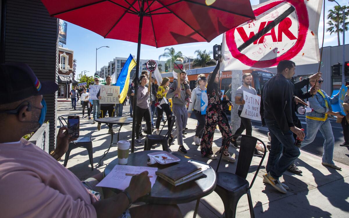A man drinks his coffee as demonstrators walk by him in Hollywood.