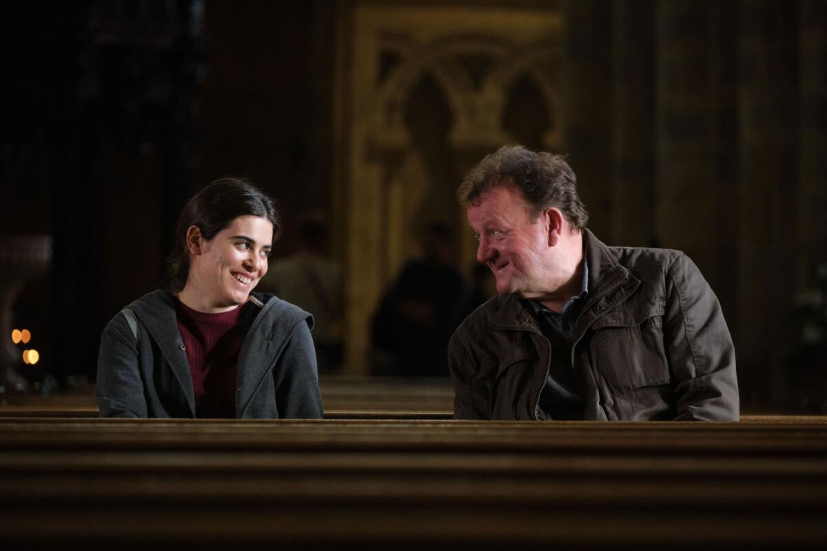 A woman and a man sit talking and smiling in a church pew.