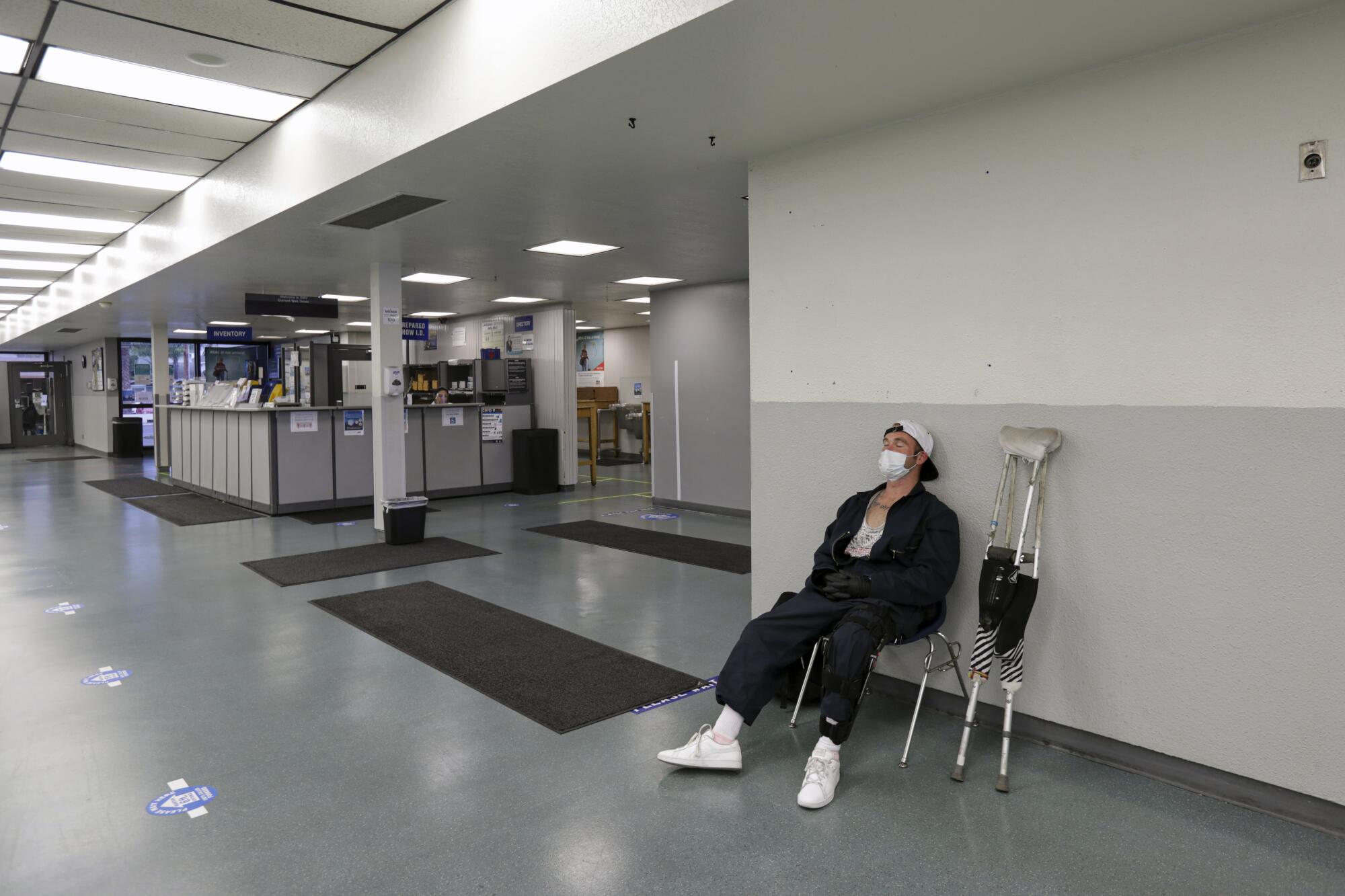 A man dozes off sitting in an chair next to a pair of crutches inside an empty DMV field office