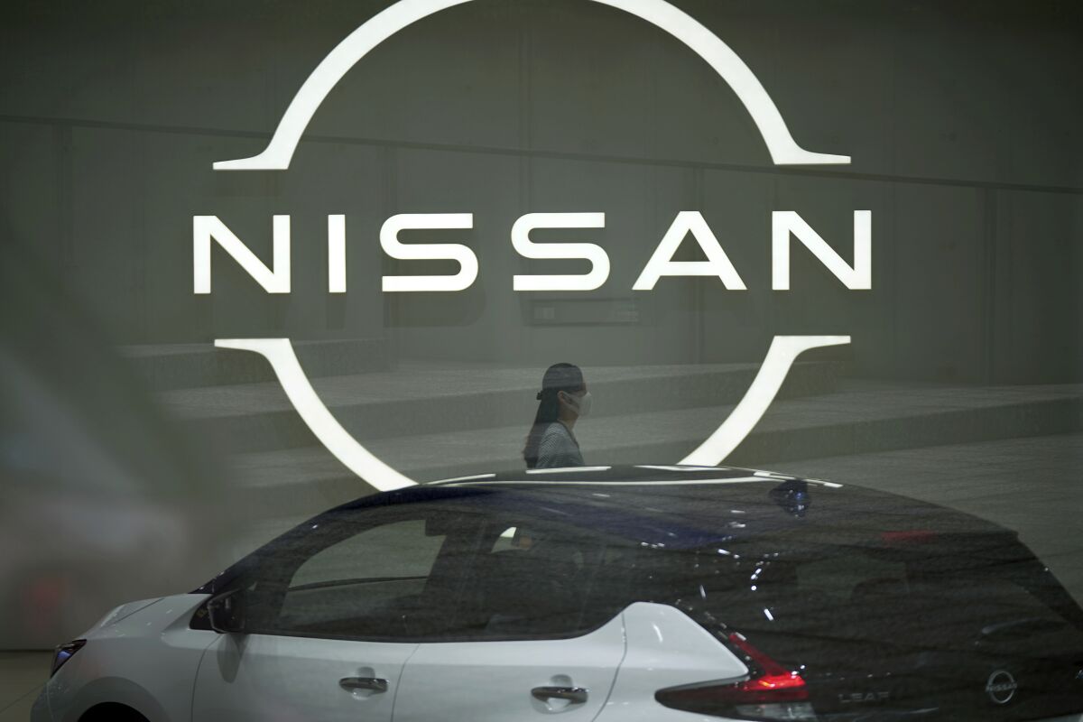 FILE - A staff walking near a Nissan logo at Nissan headquarters is seen though a window on May 12, 2022, in Yokohama near Tokyo. Nissan and Renault have changed their mutual cross-shareholdings to the same 15%, ironing out a source of conflict in the Japan-French auto alliance. (AP Photo/Eugene Hoshiko, File)