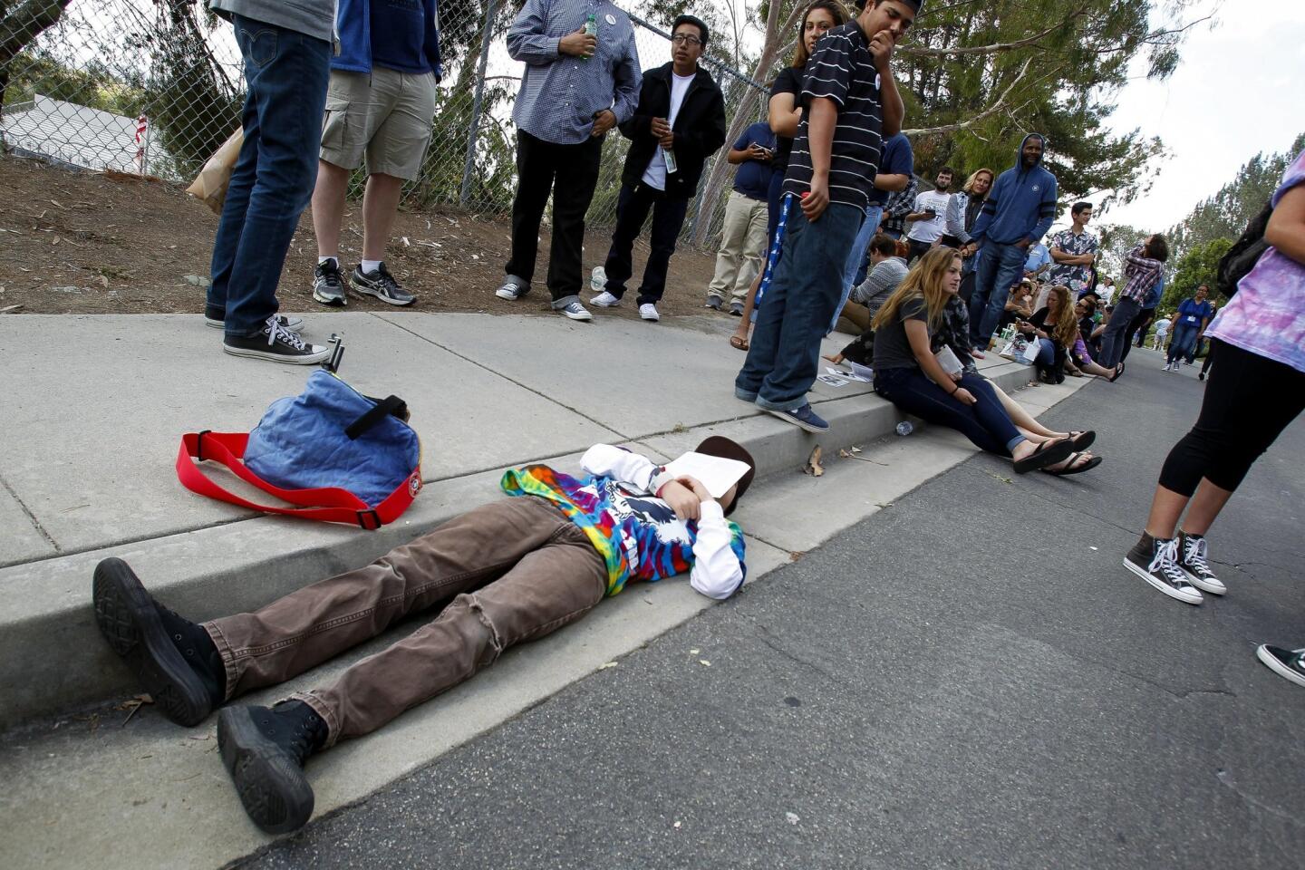 Ten-year-old Jack Rasor, who had been waiting since 8 a.m., lies in the gutter and he and others stand in line to see Democratic presidential candidate Bernie Sanders.