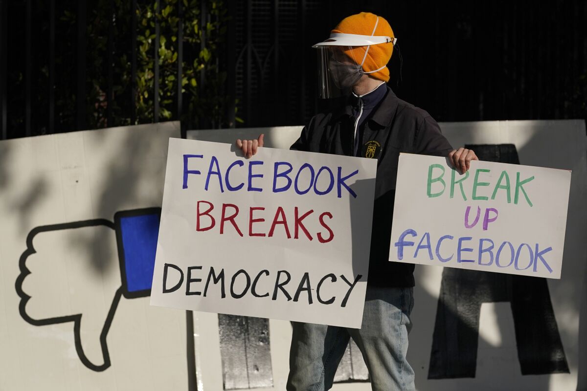 A demonstrator holds signs reading "Facebook breaks democracy" and "Break up Facebook."