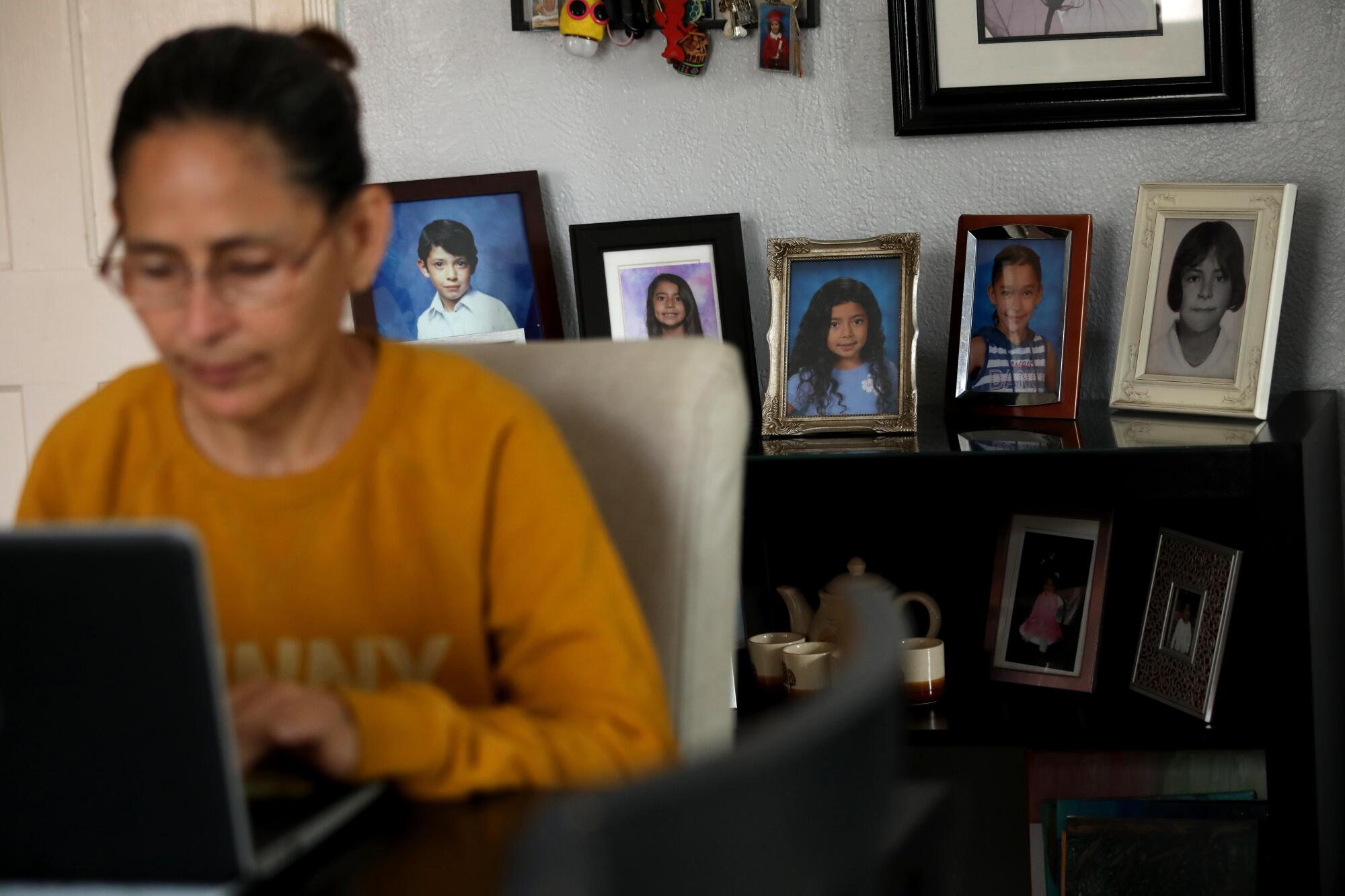 Claudia Aleman works on her computer with a backdrop of photos of her family