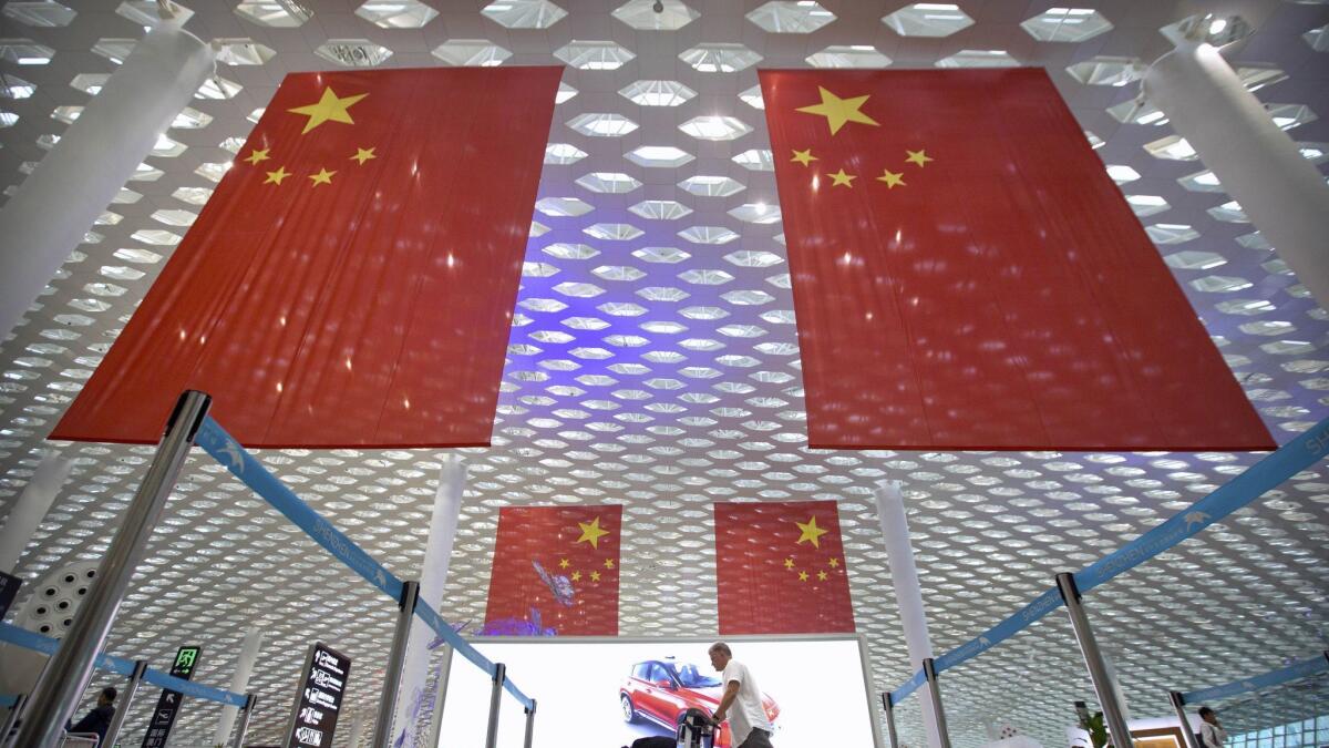 A traveler pushes his luggage beneath Chinese flags at the international airport in Shenzhen, China, on Wednesday.
