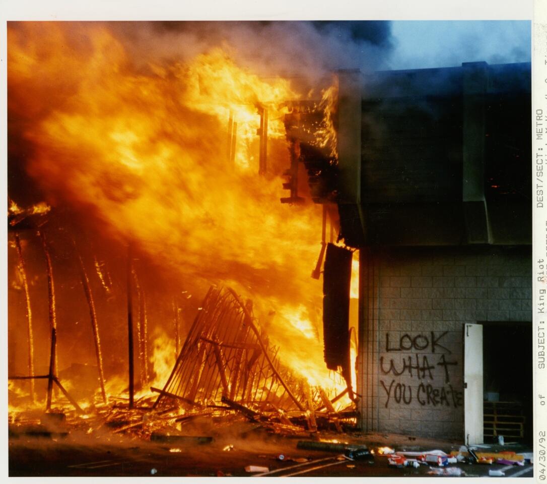 A shopping mall at the intersection of La Brea and Pico is engulfed in flames.