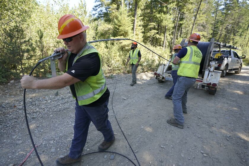 FILE - Carl Roath, left, a worker with the Mason County (Wash.) Public Utility District, pulls fiber optic cable off of a spool, as he works with a team to install broadband internet service to homes in a rural area surrounding Lake Christine near Belfair, Wash., on Aug. 4, 2021. Federal officials announced plans Thursday, July 28, 2022, to spend $401 million in grants and loans to expand the reach and improve the speed of internet for rural residents, tribes and businesses in 11 West and Central U.S. states. (AP Photo/Ted S. Warren, File)
