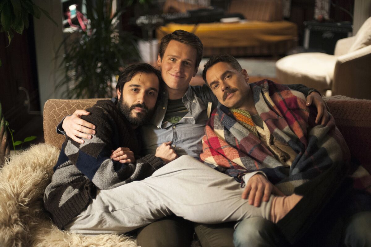 Three men cuddling together on a couch, facing the camera.