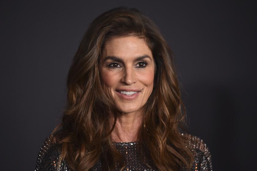 Cindy Crawford smiling against a dark background wearing a sparkling dress