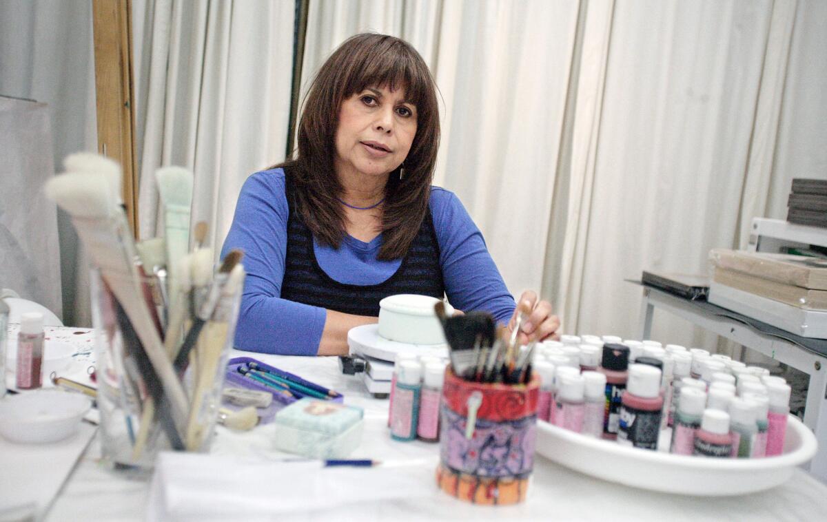 A woman in a purple shirt sits before a table with art supplies. 