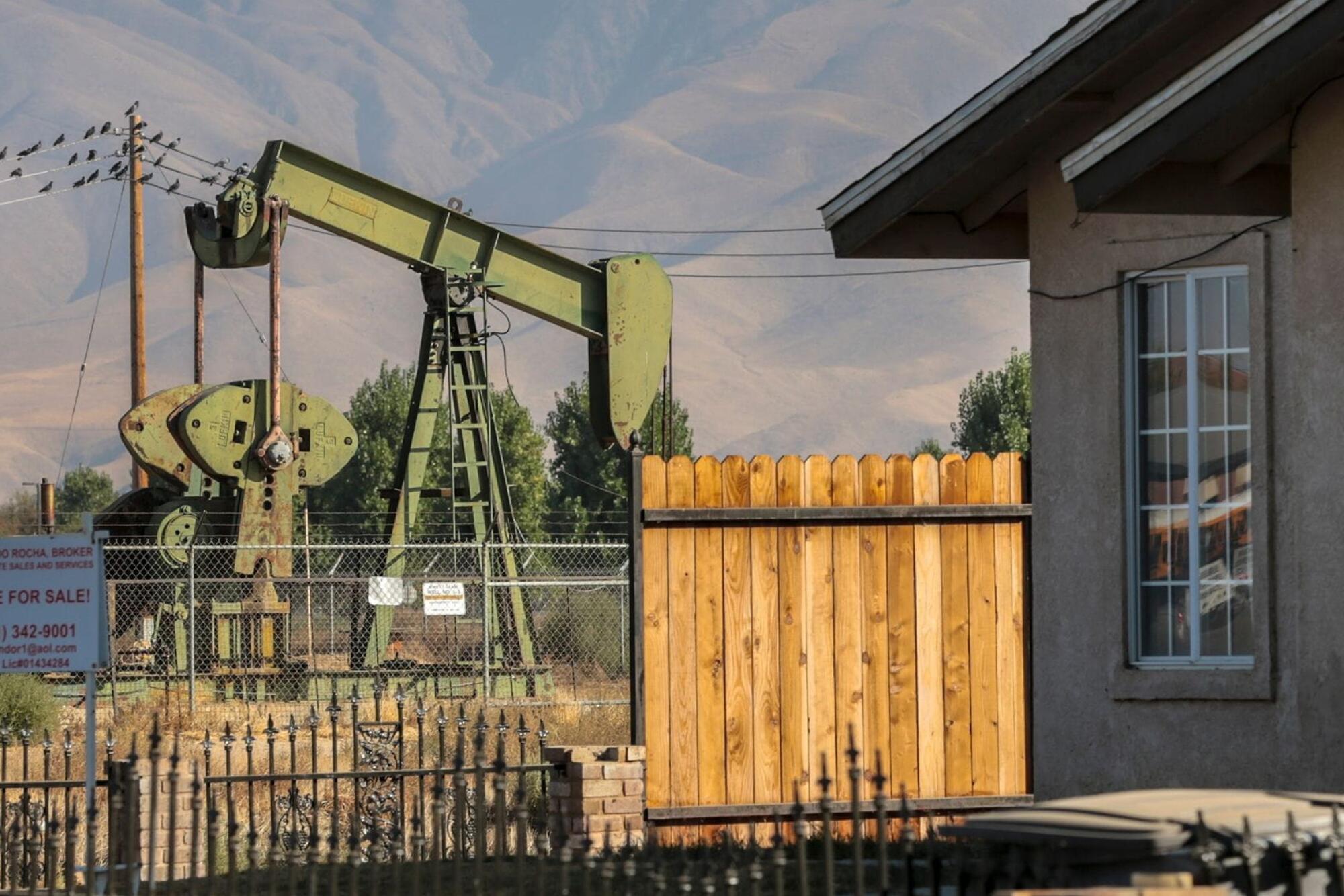 Idle oil well behind a fence near a house.