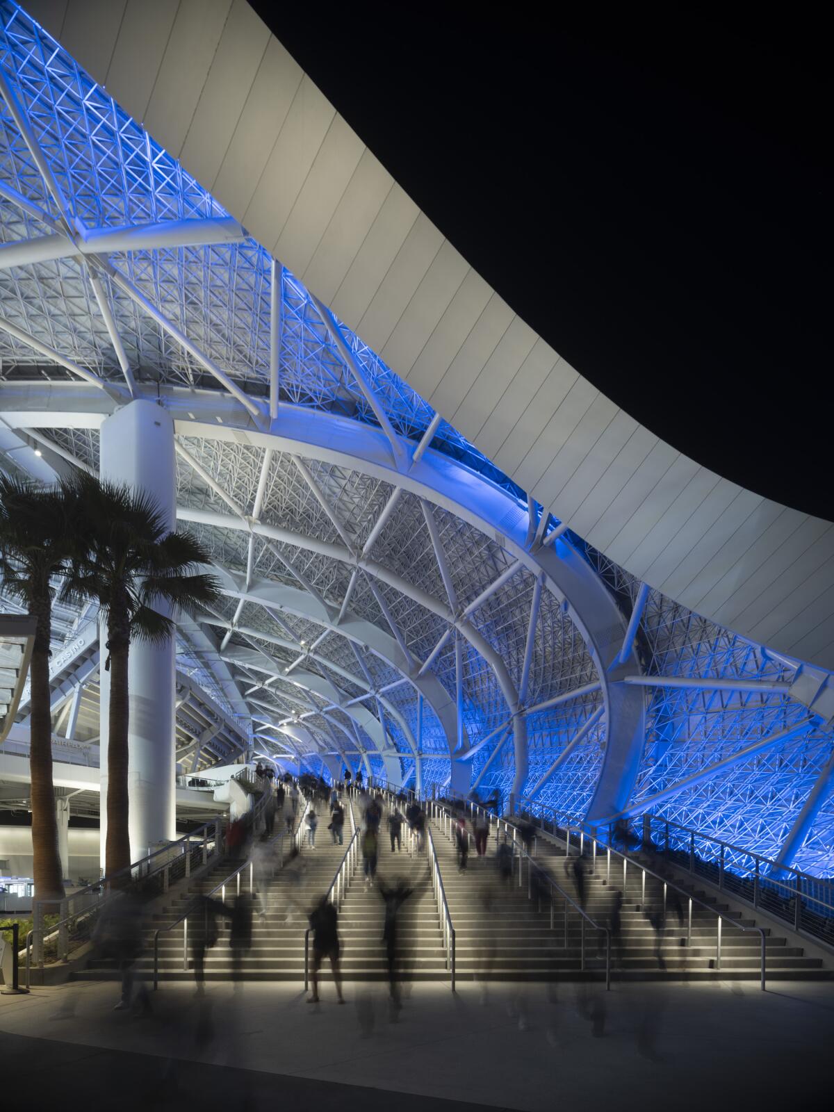 A view of a grand staircase entryway at SoFi Stadium illuminated in blue light at night.