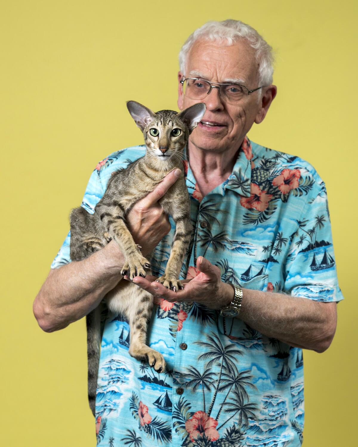 Ken Kershaw, wearing a Hawaiian shirt, holds his Oriental Shorthair cat Ibeeza Little Dragon.