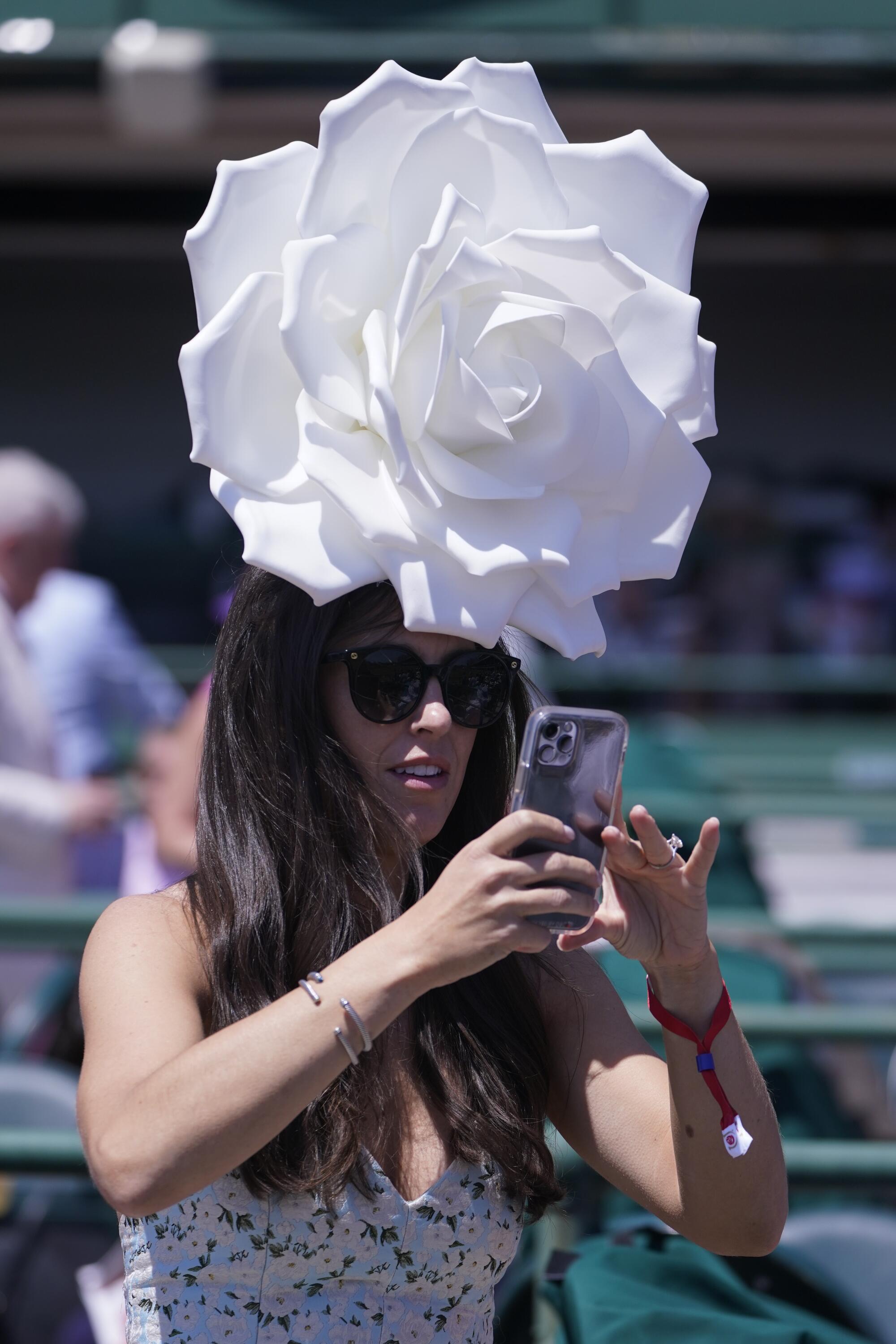 A woman takes a photo while wearing a large white rose-shaped hat.